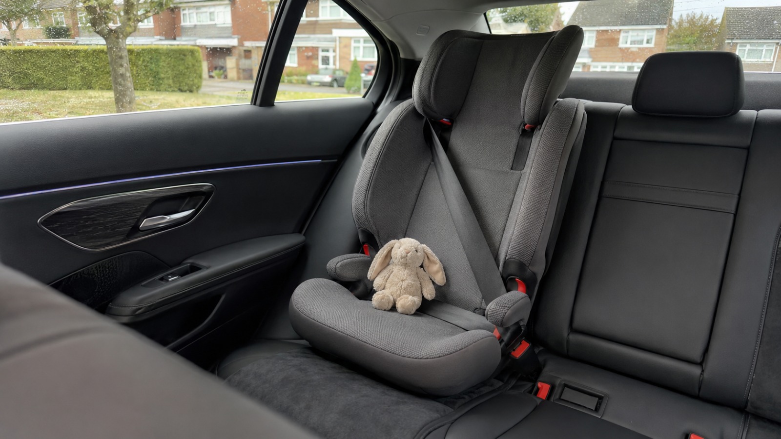 Empty grey high-back child seat fitted and seatbelted in the rear of a clean UK saloon taxi