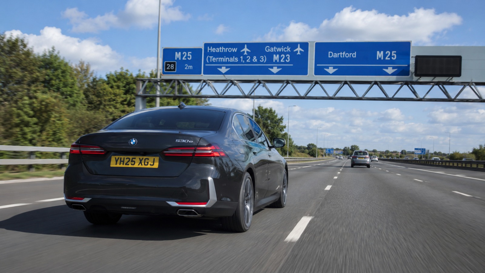 Dark saloon taxi on the M25 passing an overhead motorway gantry sign heading south toward Gatwick